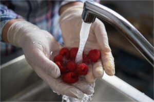 Mains avec gants lavant des framboises fruits sous l'eau du robinet