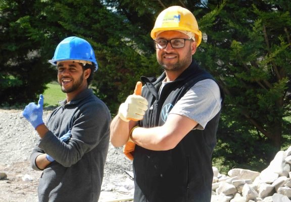 Salariés sur chantier extérieur souriants avec casque et pouce